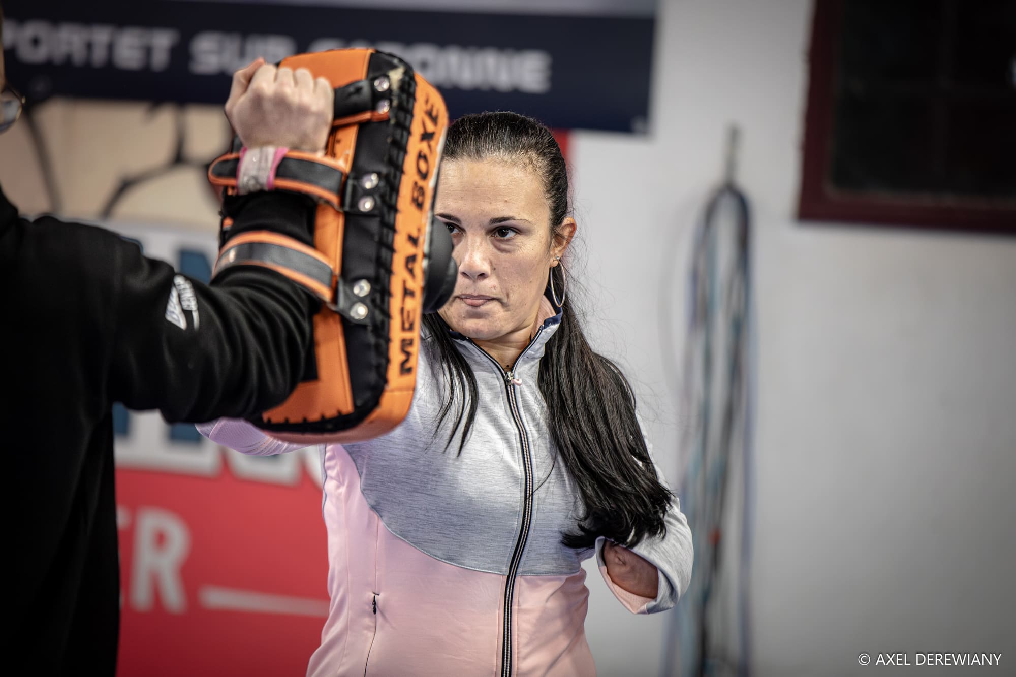 Une pratiquante en survêtement rose fixe la patte d’ours orange que le coach lui présente à hauteur de visage.